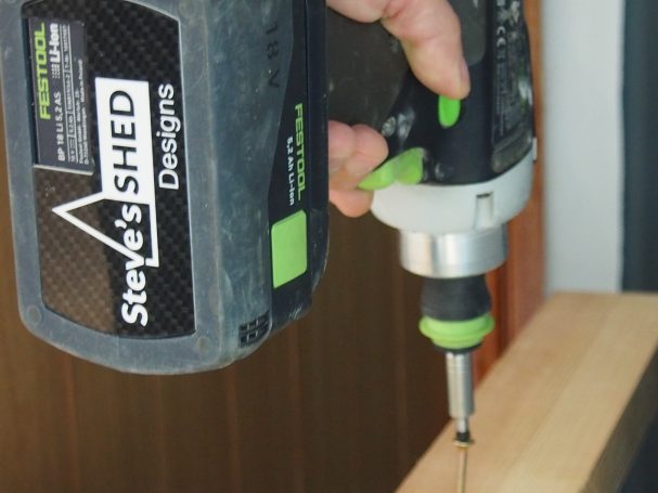 A close-up of a hand using a cordless screwdriver on wooden material.