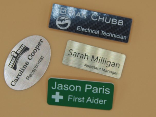 Four name badges displaying job titles: Electrical Technician, Assistant Manager, Photographer, First Aider.